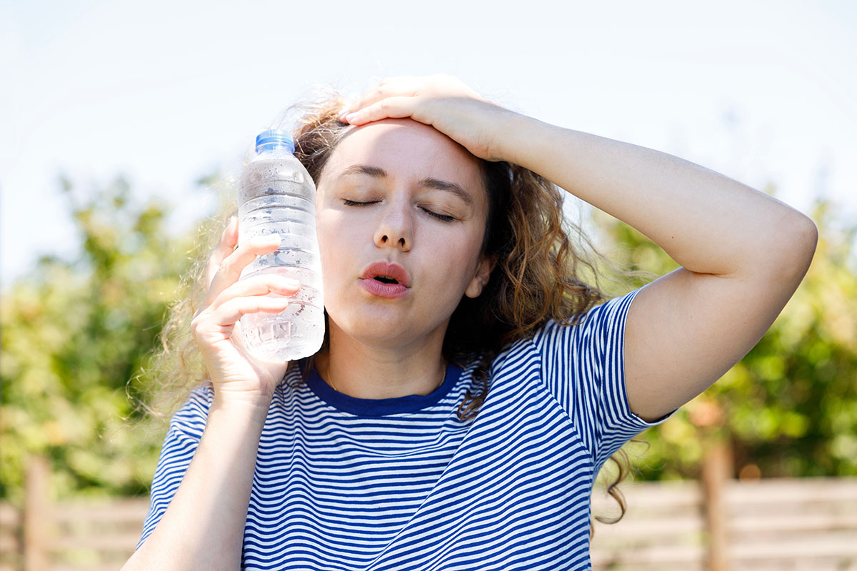 Woman outdoors with dehydration holding a water bottle to face